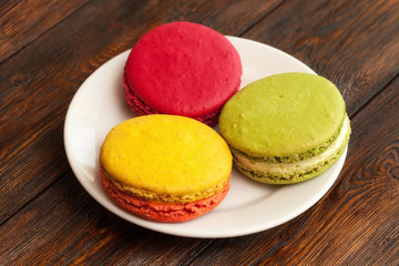 Three traditional french colorful macarons on plate, wooden background