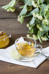 Linden tea in glass cup and jar with honey with linden flowers on a dark wooden background