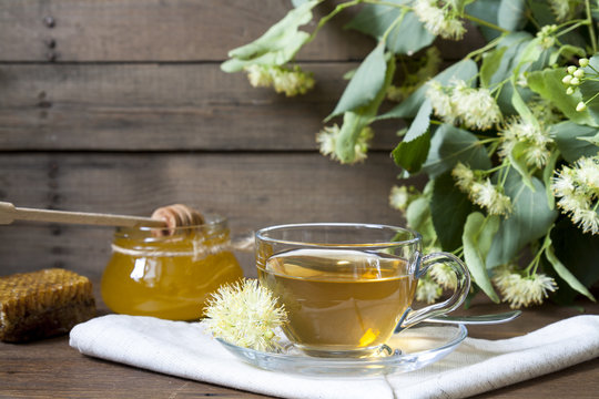 Linden tea in glass cup and jar with honey with linden flowers on a dark wooden background