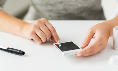close up of woman with smartphone doing blood test