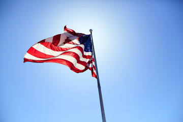 Fototapeta premium American flag blowing wind on a sunny day on blue sky background.