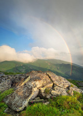 Rainbow under mountain ridge. Beautiful natural landscape in the summer time