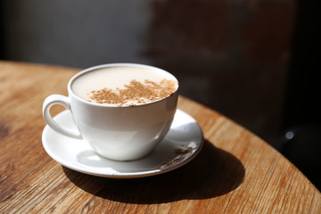 Cup of tasty latte is standing on the wooden textured table with the brick wall background.  Latte is in the white big cup.