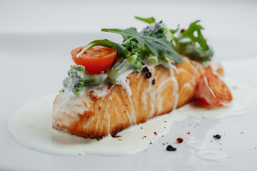 red fish in white sauce with tomatoes, broccoli and greens on white background