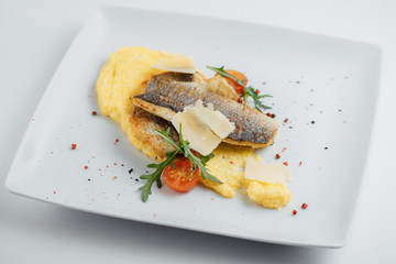 Fried fish, cheese, tomatoes and mashed potatoes on a white plate