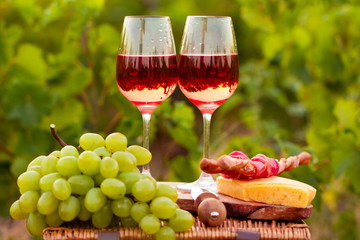 Two glasses of rose wine with meat, grape, bread and cheese on t