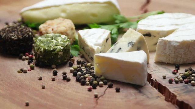 Varieties of cheese with herbs and peppercorns on a wooden board, rotating