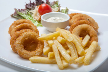 Close up of french fries and battered onion rings with sauce on a white plate decorated with lettuce leaves and cherry tomatoes