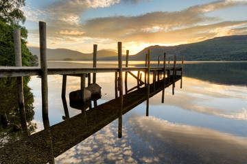 Beautiful golden sunrise with wooden jetty reflections in lake at Derwentwater, Lake District.