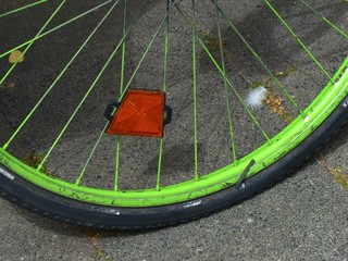 Felge mit Speichen hellgrün bemalt mit Speichenreflektor des alten Fahrrad auf grauem Asphalt bei...