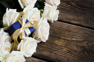 White roses with gift box on a wooden table, holiday background