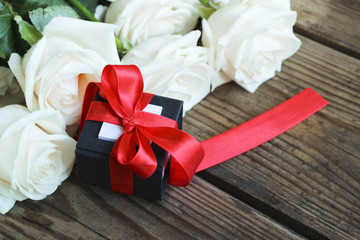 White roses with gift box on a wooden table, holiday background