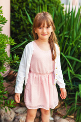 Outdoor fashion portrait of a cute little girl wearing pink dress and white jacket