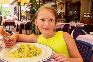 Adorable little girl eating spaghetti with avocado sauce in a restaurant