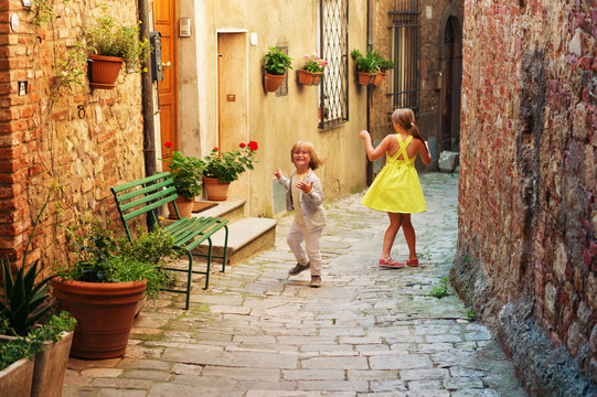 Fototapeta Adorable kids having fun outdoors, dancing on the streets of old italian city
