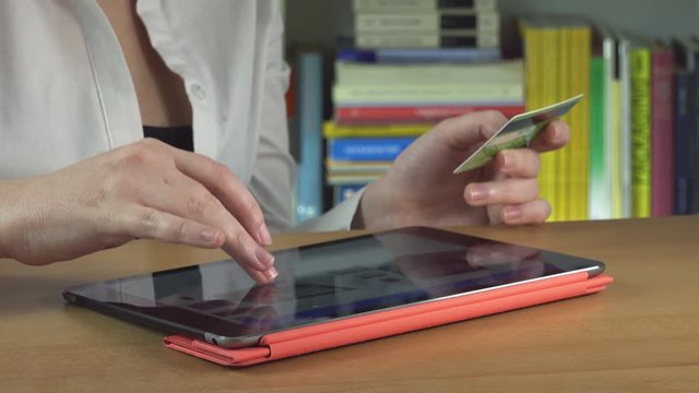 woman holding a credit card and making a purchase online using tablet computer
