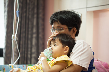 The boy wearing oxygen mask in hospital ward, boy's father's lap