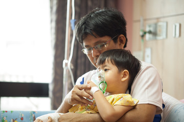 The boy wearing oxygen mask in hospital ward, boy's father's lap