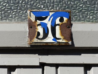 Verrostetes Blechschild mit der Hausnummer 56 und blauem Klebeband bei Sonnenschein an einem Altbau...