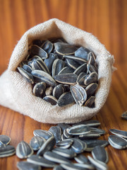 Pile of sunflower seeds in the brown small sack on the brown wooden background.Select a focal point.