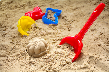 red toy shovel and colorful plastic molds in a sandbox or at the beach