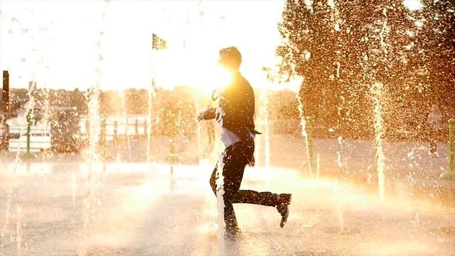happy young business man dancing in the rain outdoors at sunset. slow motion