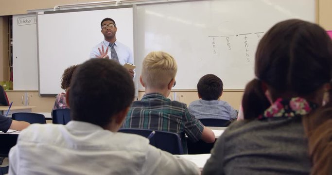 Kids watch teacher in math class, back view, 
