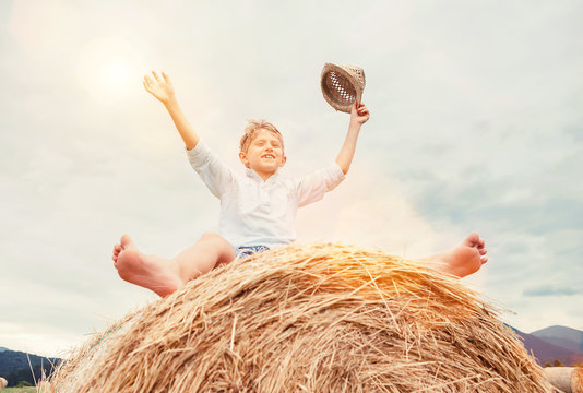 Happy boy sits over big rolling haystack