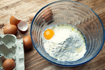 The image of eggs and flour on a wooden table.