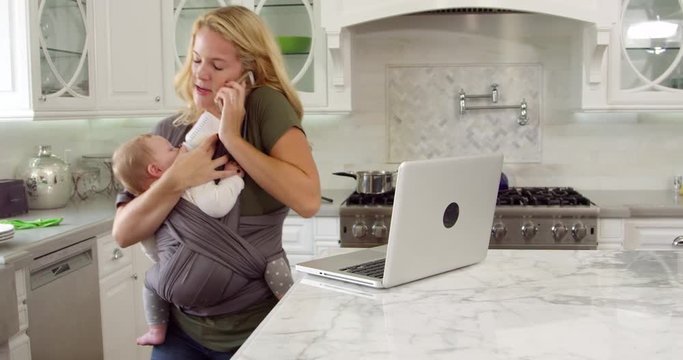 Busy Mother With Baby In Sling At Home 