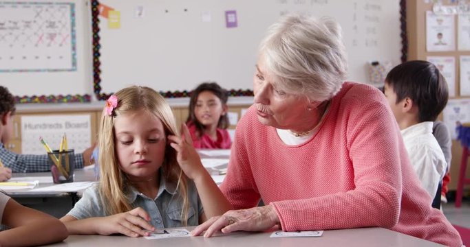 Teacher helping young schoolgirl learn time telling in class