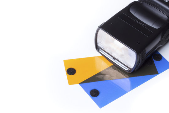 Head of a camera flash, over a white background with two gels, orange (CTO) and blue (CTB).