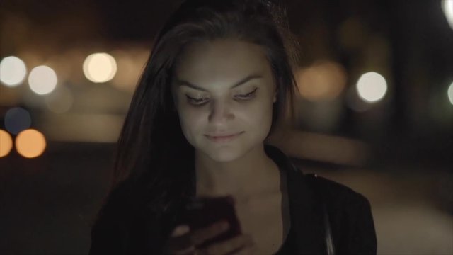 young women walking and texting on smart phone in the city at night