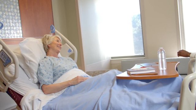 Doctor Talks To Senior Patient In Hospital Bed 