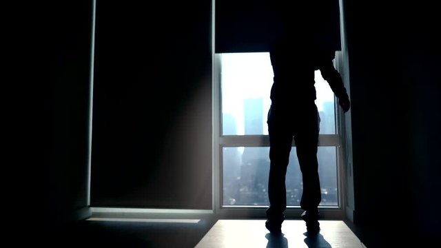 silhouette of man in modern office in the city standing on large window front