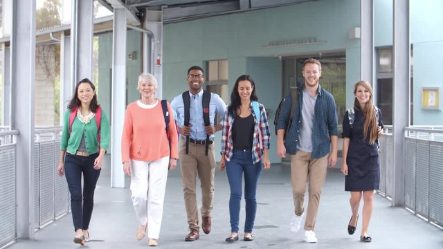 Group of smiling teachers walk in a corridor towards camera