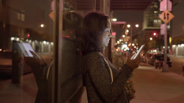 young black women standing on street in the city at night using tablet pc