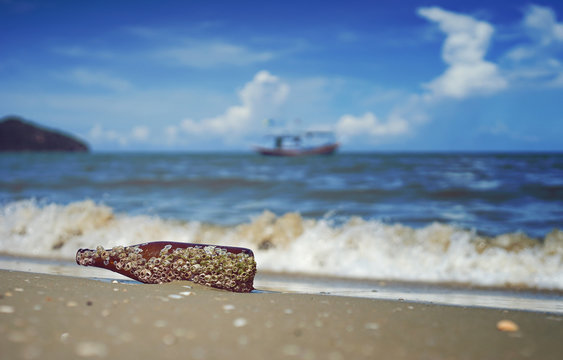 sea acorn colony on a brown glass bottle dumped pollute at the sand beach,blurred splash of sea wave and blue sky in background,filtered image,selective focus