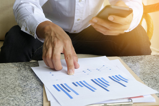 businessman holding mobile phone with analyzing financial chart
