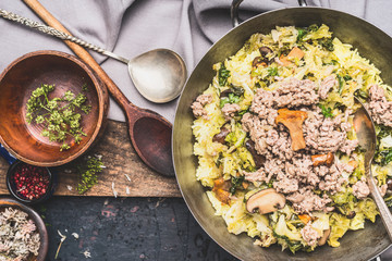 Rustic food. Dish with stewed mincemeat ,cabbage, rice and mushrooms with cooking spoons on dark vintage background , top view