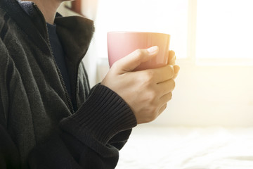 young woman hands holding hot cup of coffee in morning sunlight