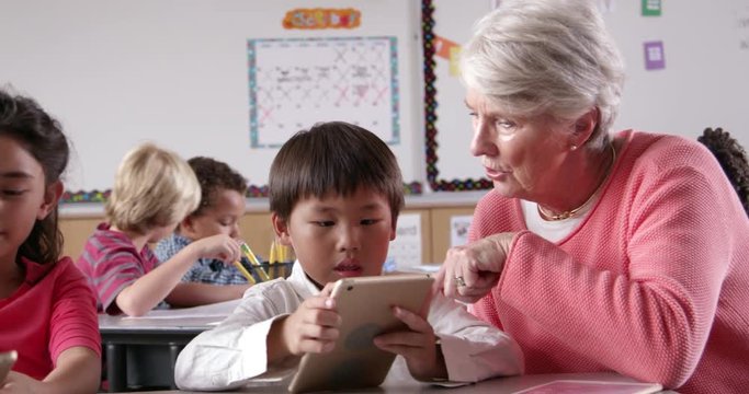 Teacher helps young kids using tablet computers in classroom
