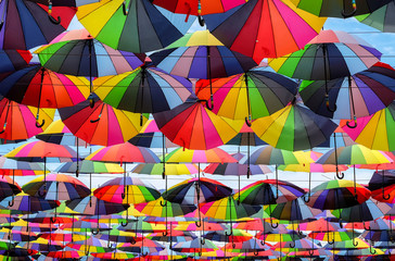 Fototapeta na wymiar Bright colorful rainbow umbrellas floating above the street, side view