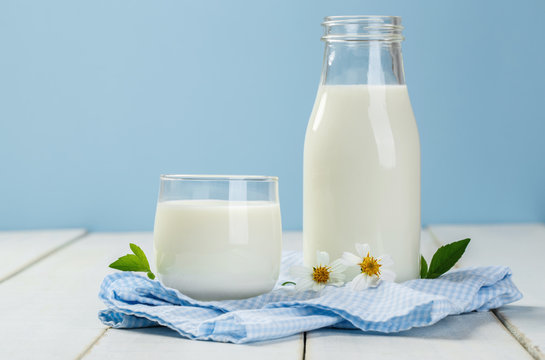 A bottle of milk and glass of milk on a white wooden table on a