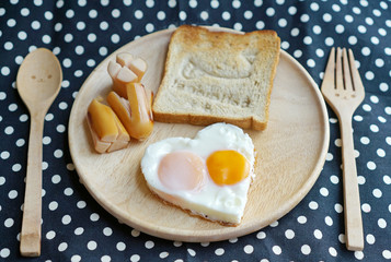 Breakfast consist of fried egg in shape of heart and happy bread