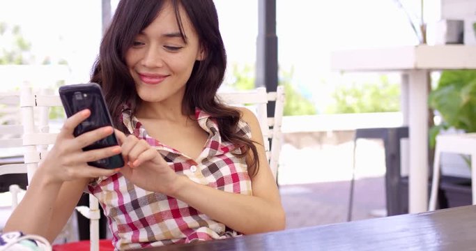 Young woman relaxing on an outdoor patio with a mobile phone reading a text message with a serious expression