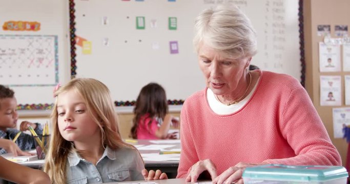 Senior teacher helping young schoolgirl in classroom