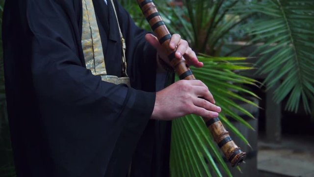 Japanese musician plays on flute in the park. Fue made of bamboo