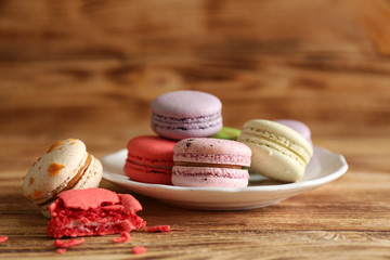 Colorful tasty macaroons in plate on wooden background