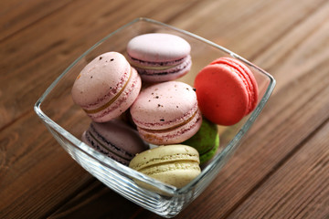 Colorful tasty macaroons in glass bowl on wooden background